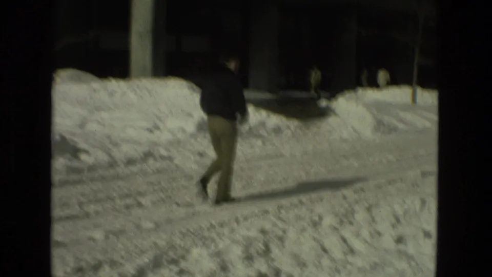 A man in a dark jacket walks across an icy, snow-banked sidewalk in the 1978 Drexel Hill winter footage.