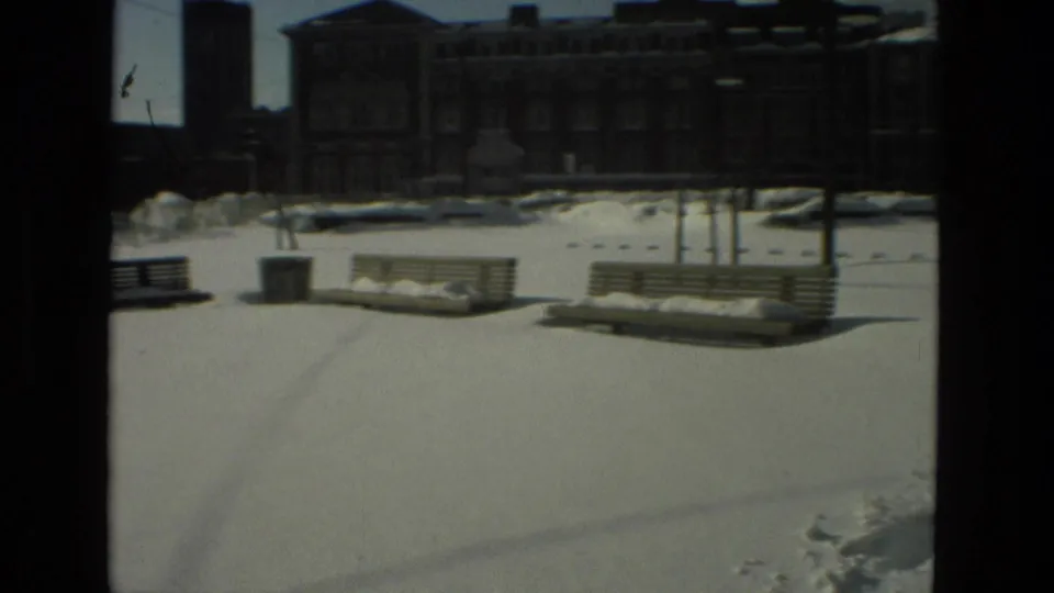 Snow blankets benches and an open public square, with larger buildings in the background in the Drexel Hill 1978 footage.