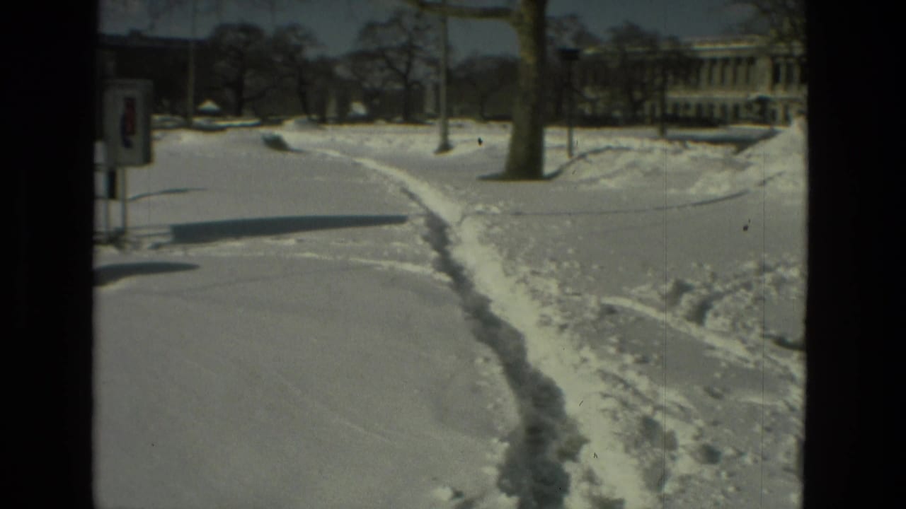 1978 Drexel Hill frame with a curved snowy footpath, poles, lampposts, bare trees, and institutional-looking buildings beyond.