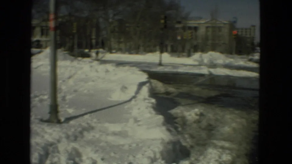1978 Drexel Hill street view showing snowbanks, a cleared path, traffic lights, bare trees, and a large building across the road.