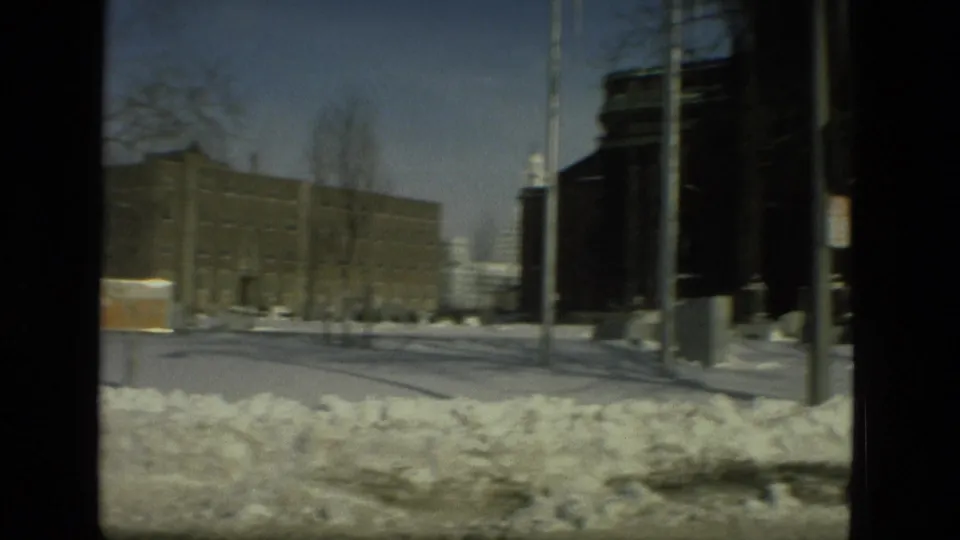 1978 Drexel Hill frame showing a snowbank beside the road, a large brick building, poles, bare trees, and winter street fixtures.