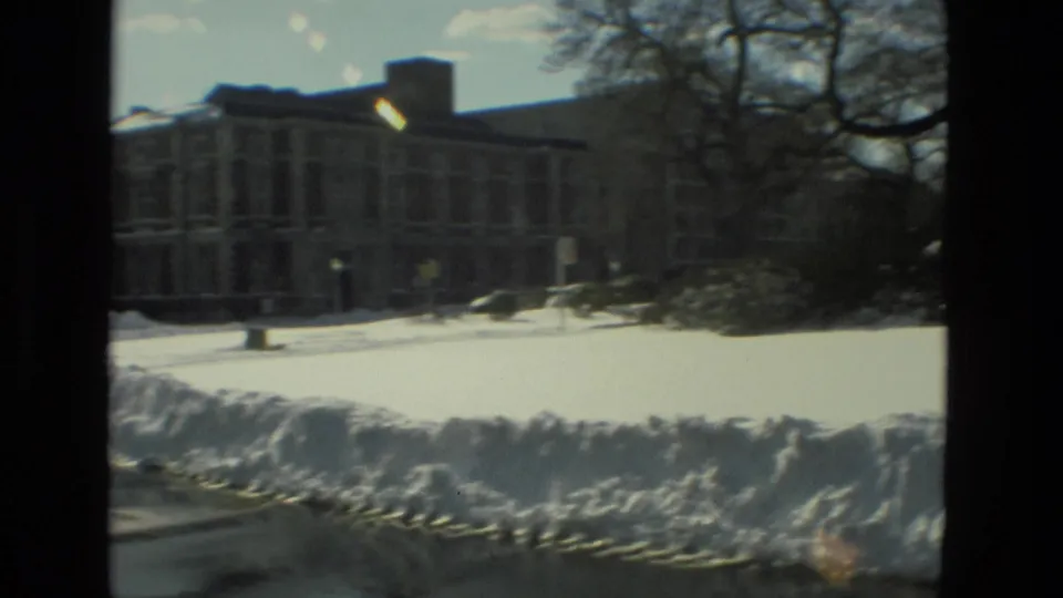 1978 Drexel Hill winter view of a large institutional-looking building beyond a snowy lawn, with bare trees and snowbanks along the road.