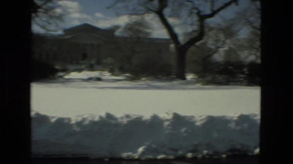 Snow-covered campus landscape in Drexel Hill, Pennsylvania, with bare winter trees and a large institutional building set back from the road.
