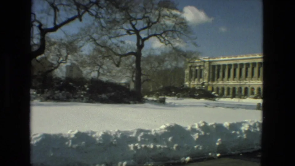 Vintage 8mm view of a long classical-style building with columns across a snow-covered campus setting in Drexel Hill.