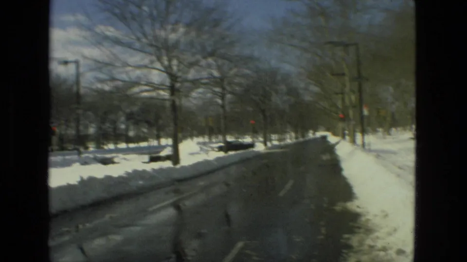 1978 Drexel Hill street view showing a plowed wet road, high snowbanks, bare trees, streetlights, and traffic signals in the distance.