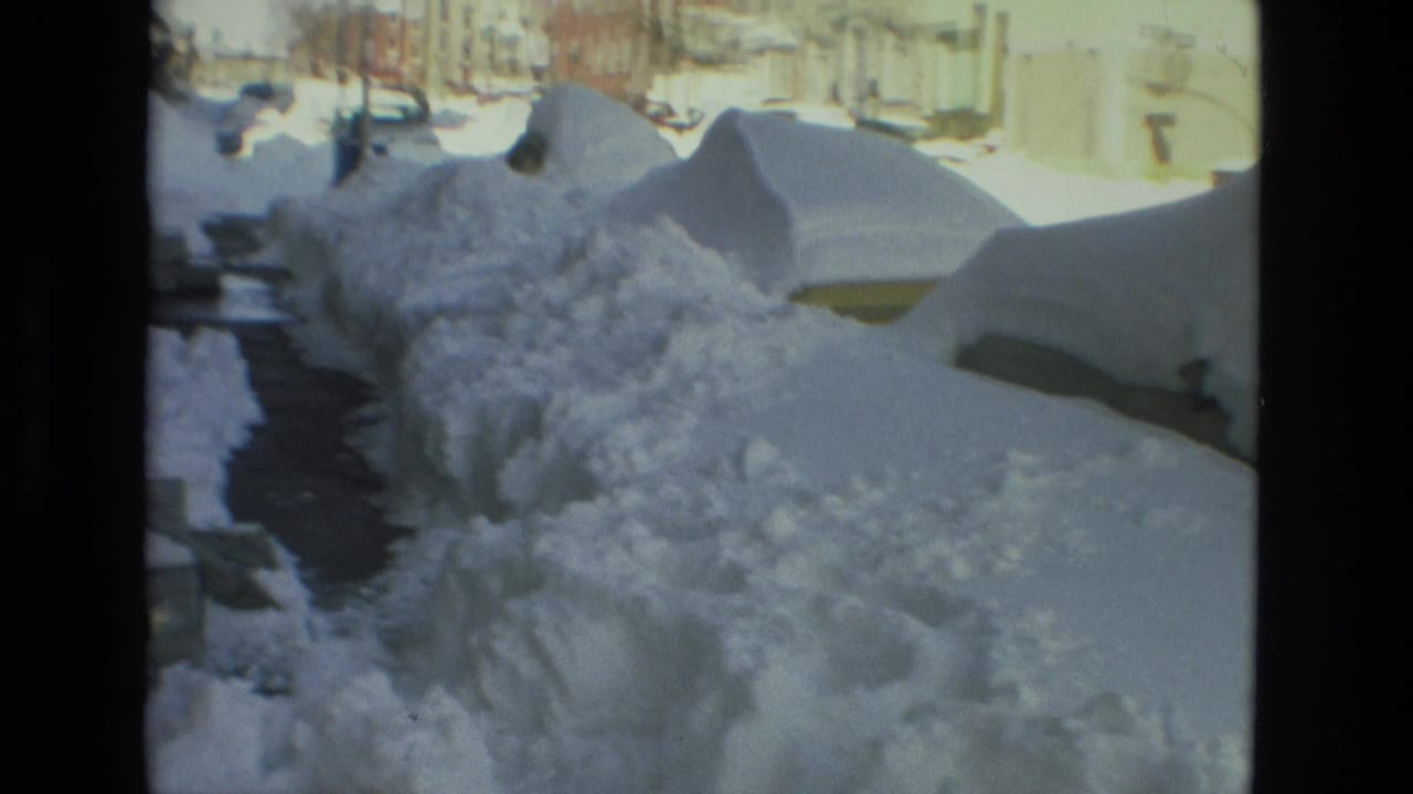 Drexel Hill, Pennsylvania residential street in 1978 with deep snowbanks, partially buried parked cars, cleared sidewalk sections, and houses beyond the snow.