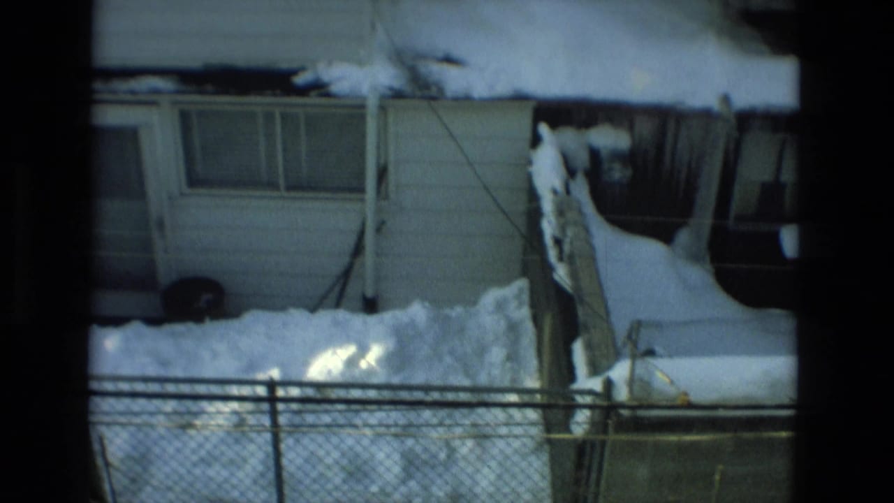 Snow-covered house exterior behind a chain-link fence and small yard.