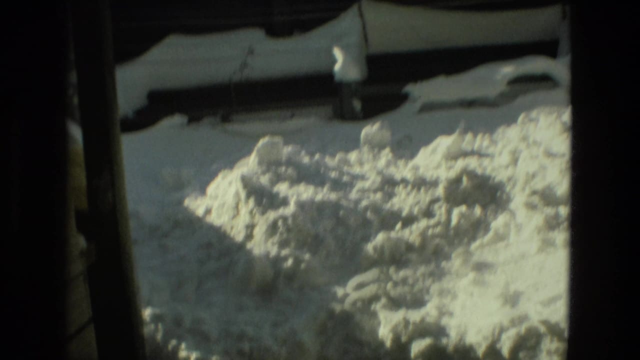 Snow piled outside a dark doorway or window, with part of a yard structure visible.