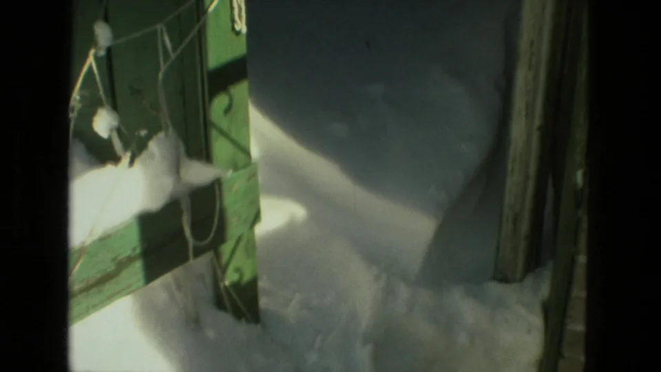 Close 8mm view of snow piled against green painted wood in a Drexel Hill residential exterior space.