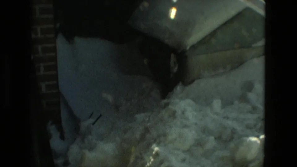 Dim 1978 Drexel Hill alley frame showing snow piled near brickwork and a covered exterior object.