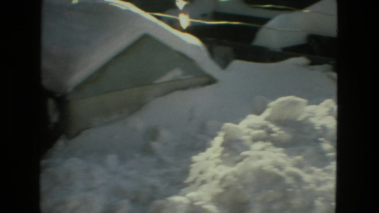 A shaky 8mm view of deep snow against a Drexel Hill residential roof and snowbank in winter light.