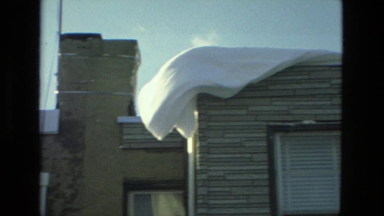 Snow piled on a roof edge beside brick and siding house exteriors.