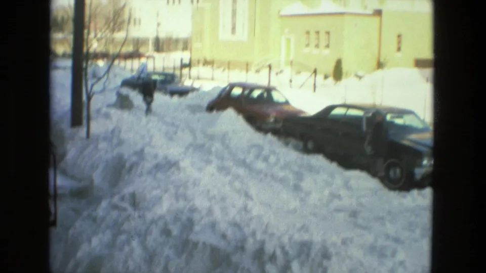 1978 Drexel Hill street view with parked cars partly surrounded by snowbanks near trees and a light-colored church-like building.