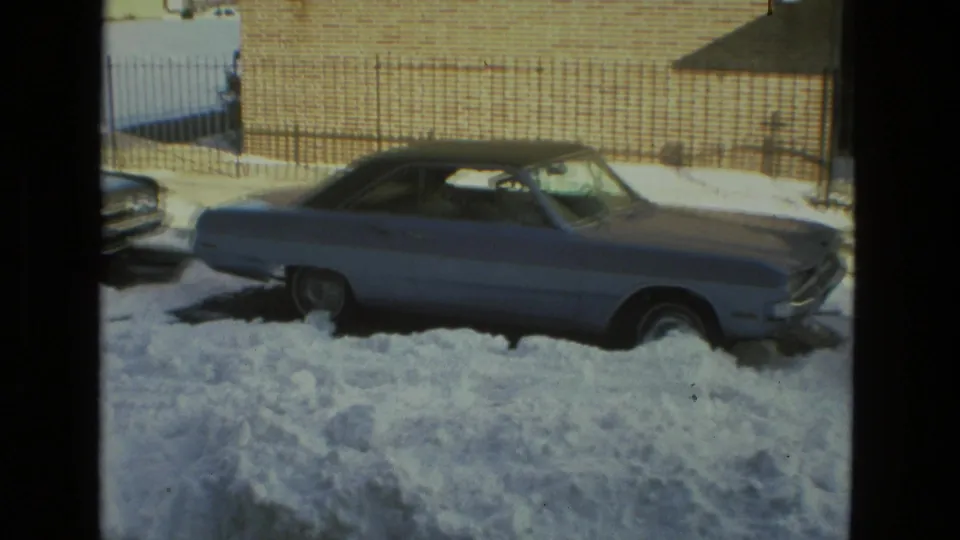 A snow-covered Drexel Hill street view shows a vintage car parked against a brick wall, with deep plowed snow in the foreground.