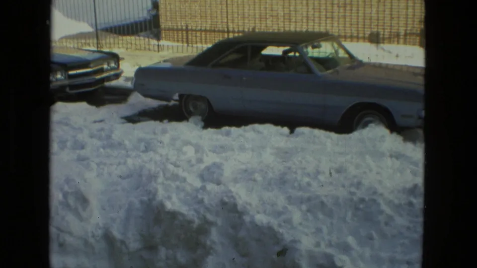 A 1978 Drexel Hill winter frame centers on a parked vintage car, deep snowdrifts, and a brick wall along the street.