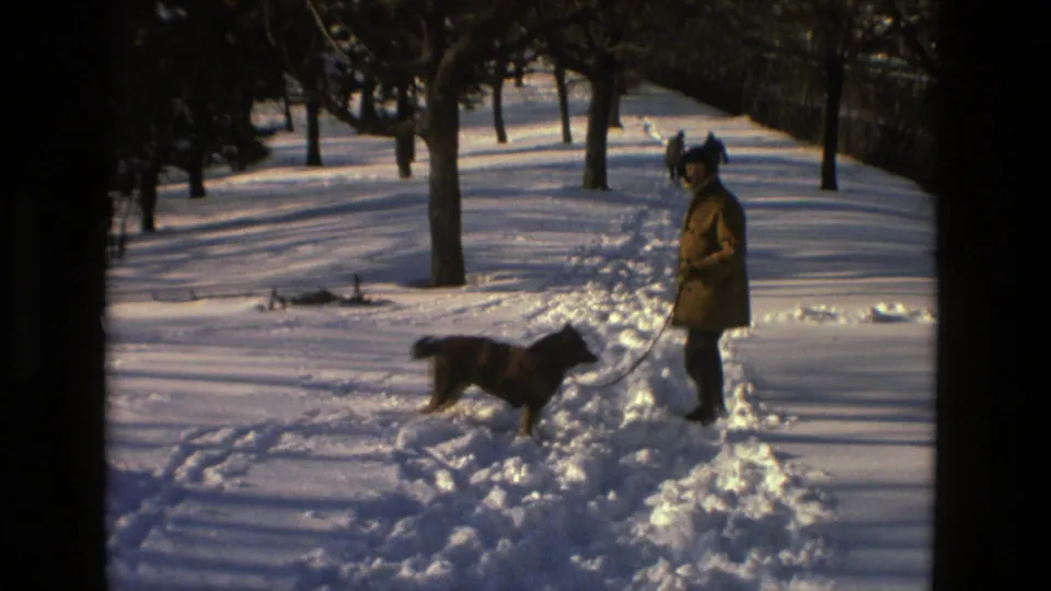 The adult and dog remain on a snowy park path in Drexel Hill, with footprints and bare trees visible in the 1978 8mm frame.