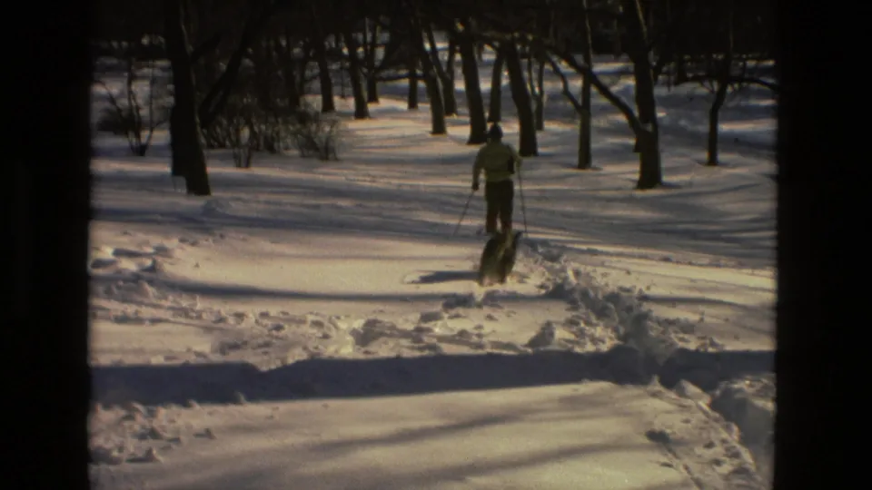 The skier and dog appear together in the snowy Drexel Hill woods, moving away from the camera in the 1978 8mm clip.