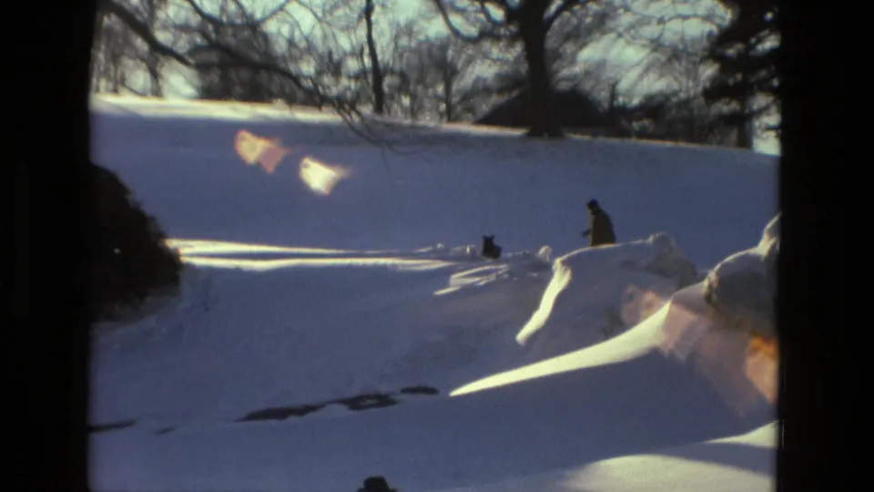 A person and dog appear small against a bright snow-covered hillside in 1978 Drexel Hill winter footage.
