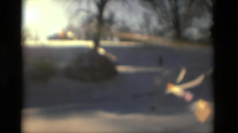 Soft-focus 8mm frame from the Drexel Hill winter scene, with snow, a distant figure, bare trees, and warm lens flare.