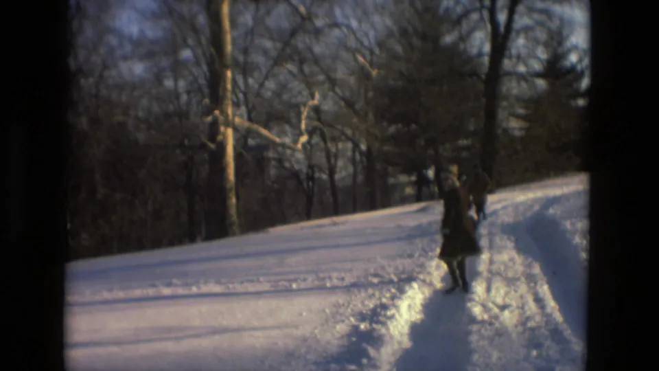 1978 Drexel Hill frame showing two adults walking together along tracks in the snow near leafless trees.