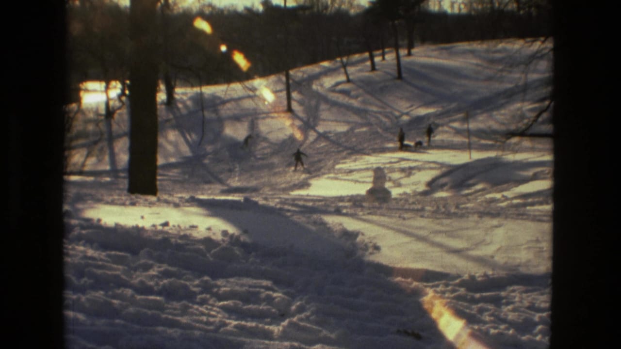 Snow-covered slope with several distant people near trees and a small snowman.