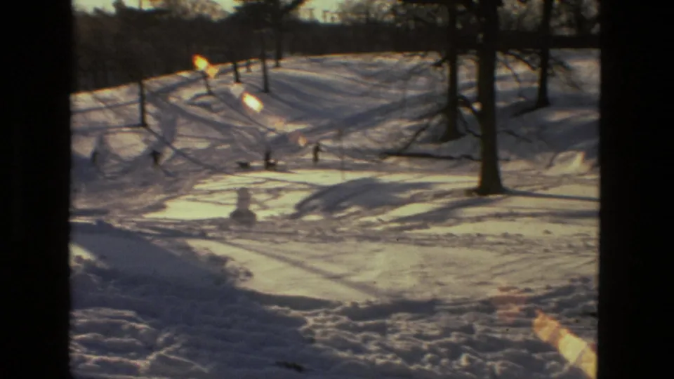 1978 Drexel Hill 8mm frame showing distant figures on a snowy hill, a small snowman, tree shadows, and bright winter light.