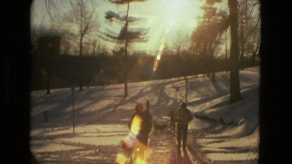 People appear on a snowy Drexel Hill park path in warm low sun, with bare trees and 8mm lens flare.