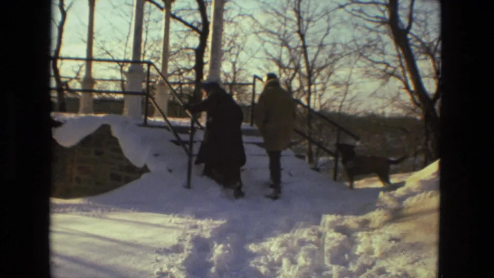 1978 Drexel Hill home-movie frame of two bundled adults walking by snow-covered steps, stonework, and railings in a park.