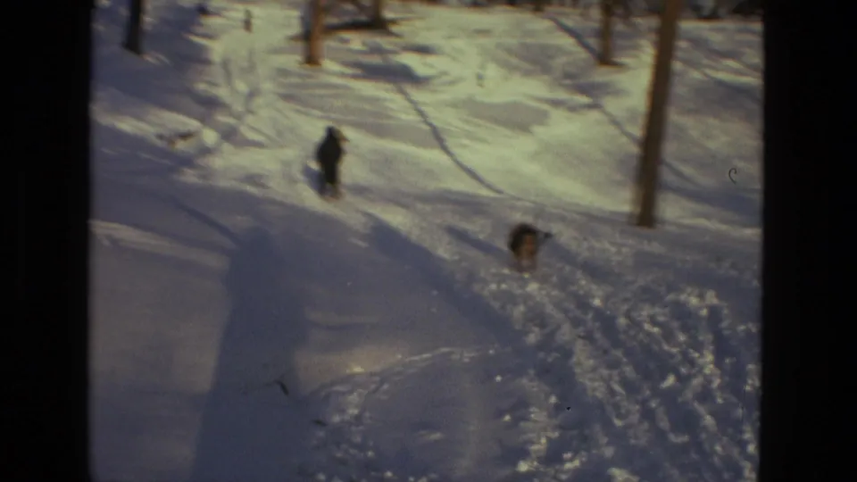 A distant child moves through deep snow in a wooded Drexel Hill setting, with tracks and bare trees visible in the 1978 home movie frame.