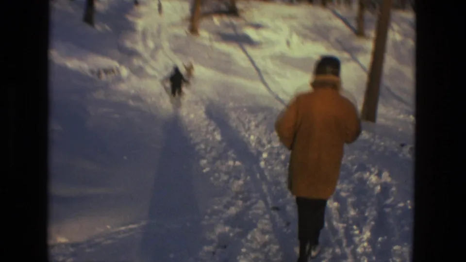 In this 1978 Drexel Hill 8mm frame, a bundled person in a tan coat walks through snow toward another figure in a wooded area.