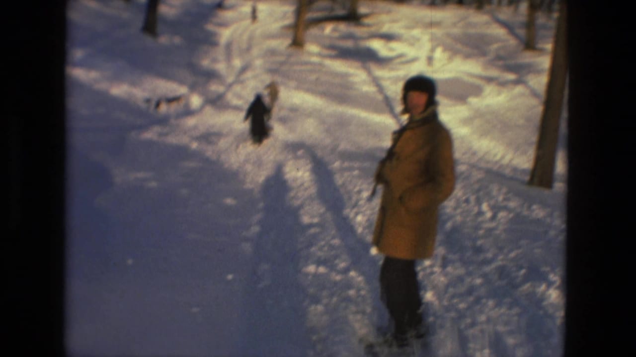 A bundled person in a tan coat pauses on the snowy path in Drexel Hill, Pennsylvania, with bare trees and tracks around them.
