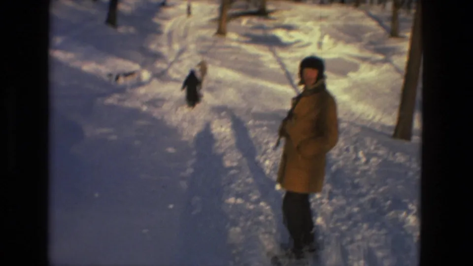 A bundled person in a tan coat pauses on the snowy path in Drexel Hill, Pennsylvania, with bare trees and tracks around them.