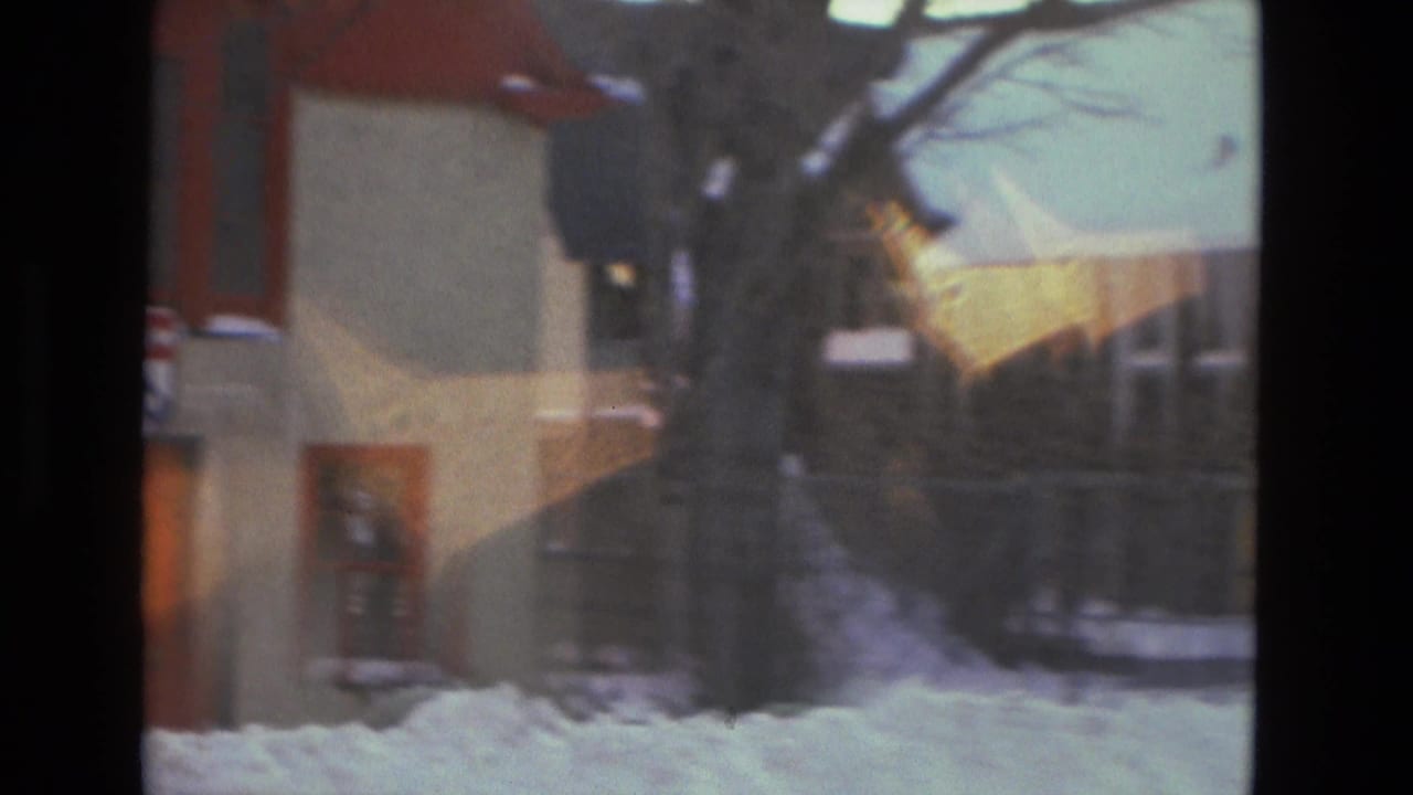 Snowy Drexel Hill street view with a residential building, bare tree, deep snow, and a pedestrian partly visible near the sidewalk.