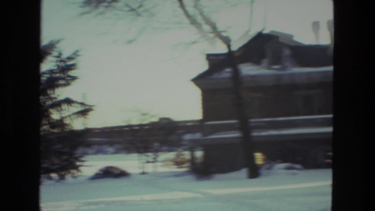 Snow-covered large house and trees seen from a moving handheld camera.