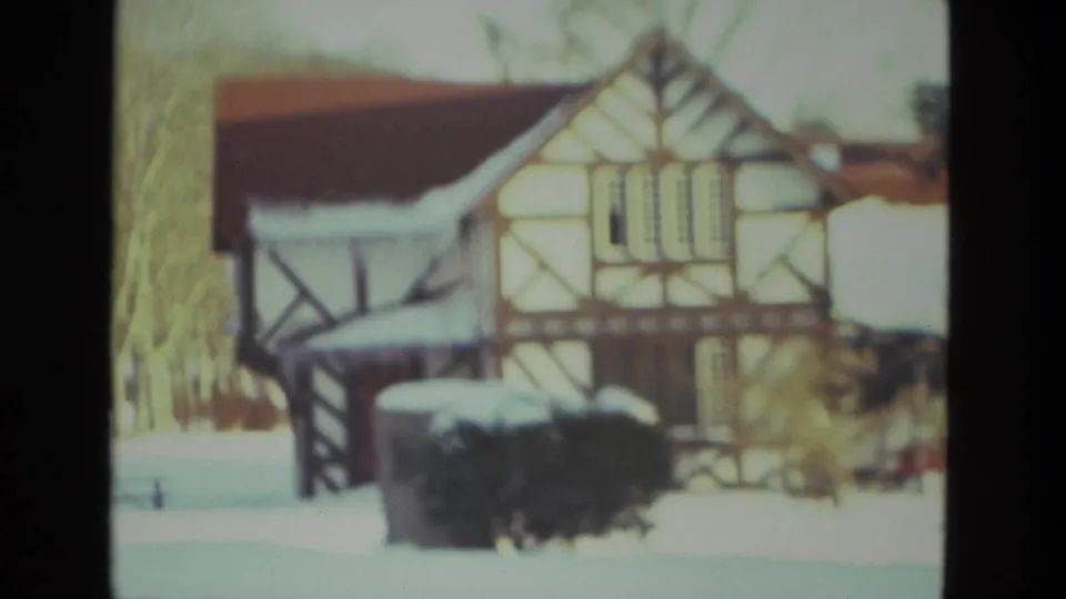 1978 Drexel Hill home-movie view of a Tudor-style house with snow on its roof, shrubs, and pale winter trees.