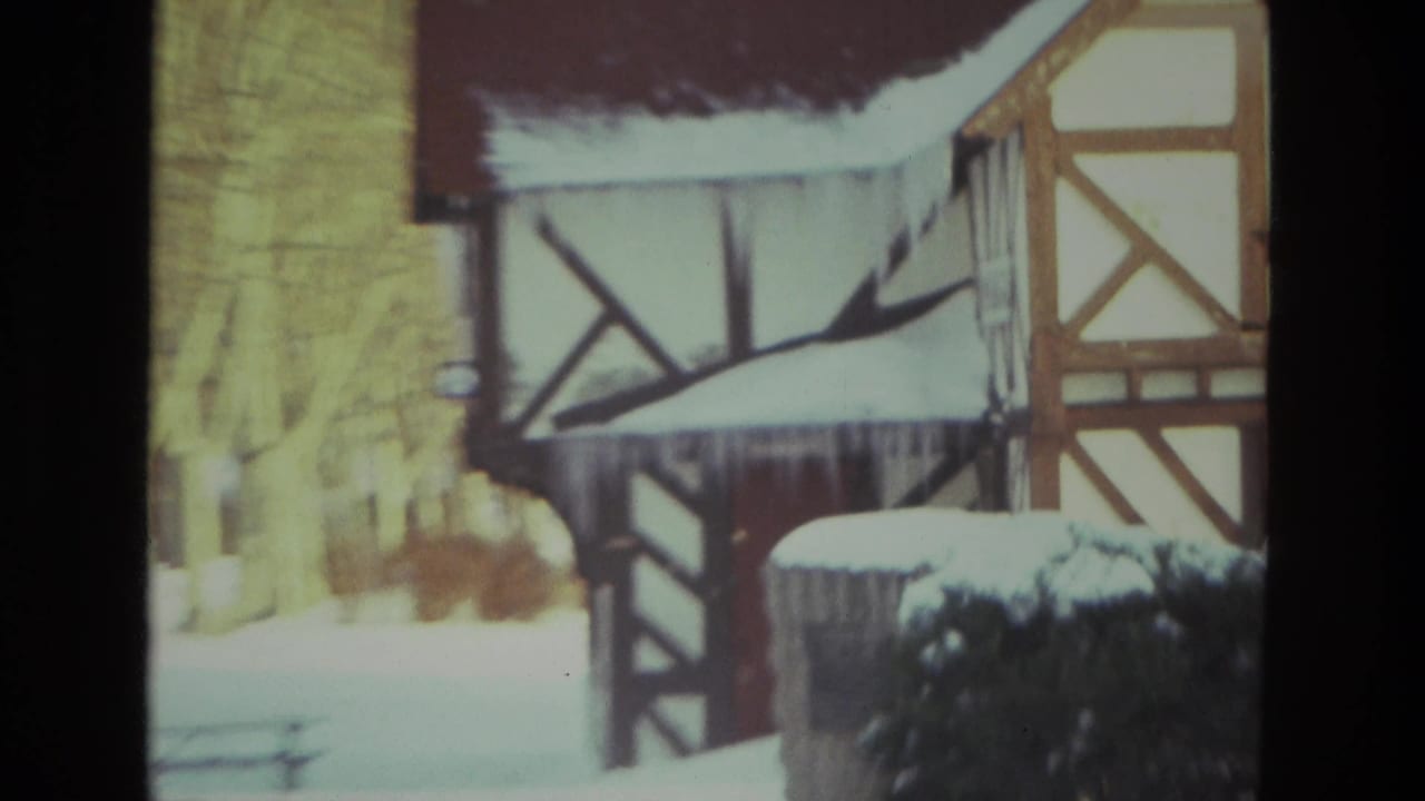 1978 Drexel Hill home-movie frame showing a snow-covered half-timbered house exterior, icicles, shrubs, and bare winter trees.