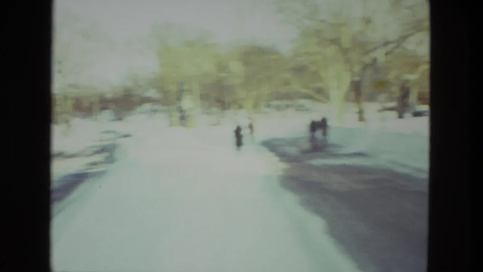 Distant figures walk through snow in a 1978 Drexel Hill home-movie view, with trees and bright winter exposure softening the scene.