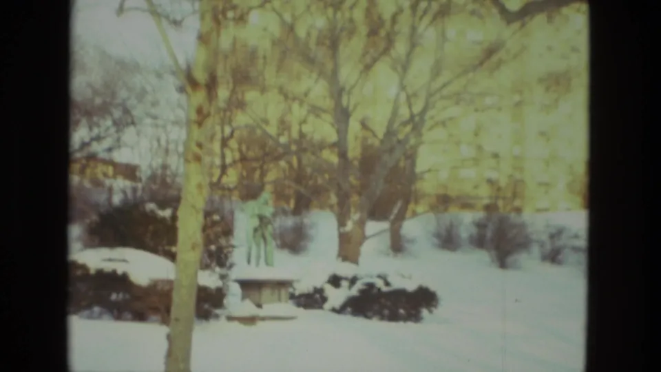 1978 Drexel Hill winter frame showing a snowy yard, bare trees, shrubs, and a small bench or low yard structure in soft Super 8 color.