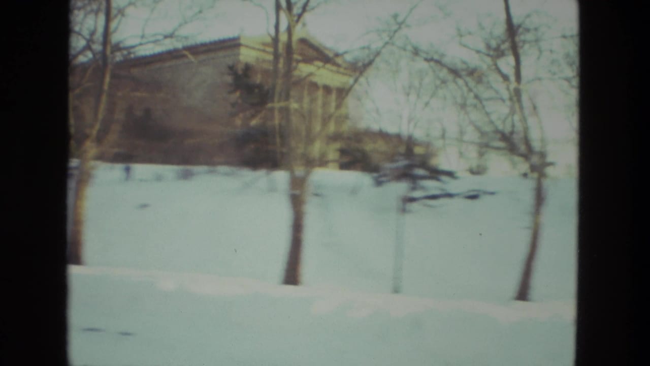 Snowy hill with bare trees and a low building partly visible at left.