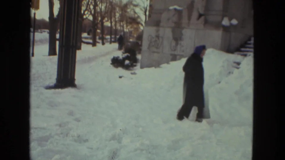 1978 Drexel Hill winter frame showing a distant person in a dark coat walking through snow near a masonry structure and bare trees.