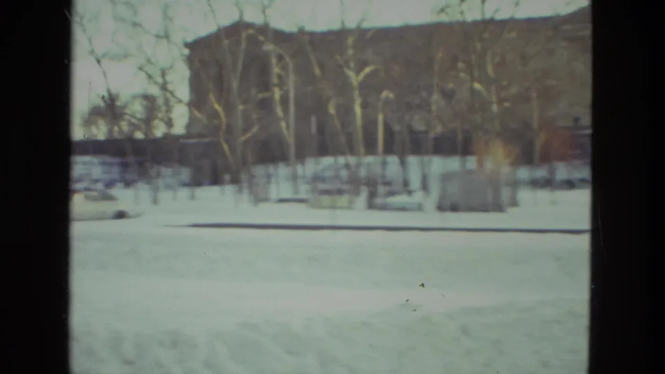 1978 Drexel Hill winter frame showing snow, leafless trees, a low fence or structure, and a darker wooded rise in the distance.