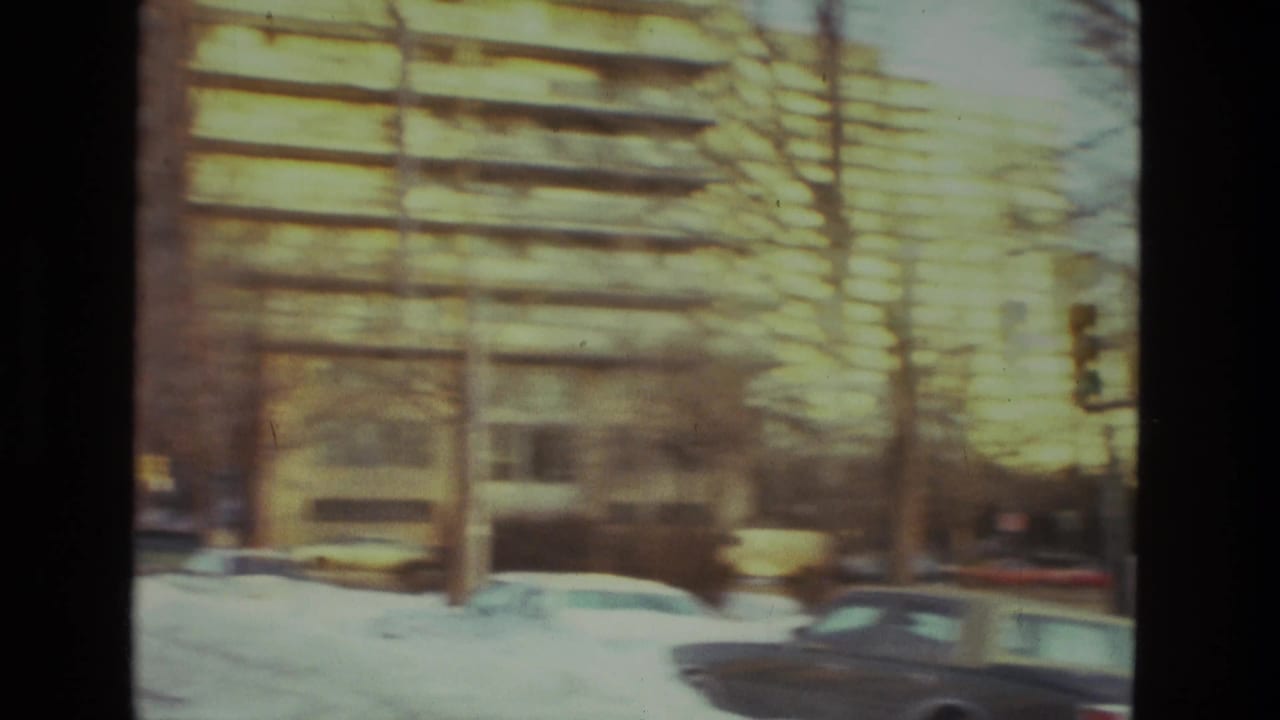 Apartment building facade beside a snowy street with parked cars in the foreground.