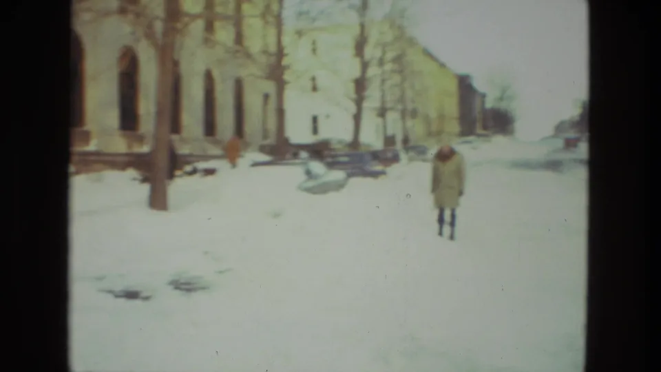 A person in a long coat walks through snow near Drexel Hill apartment buildings in the 1978 home-movie scene.