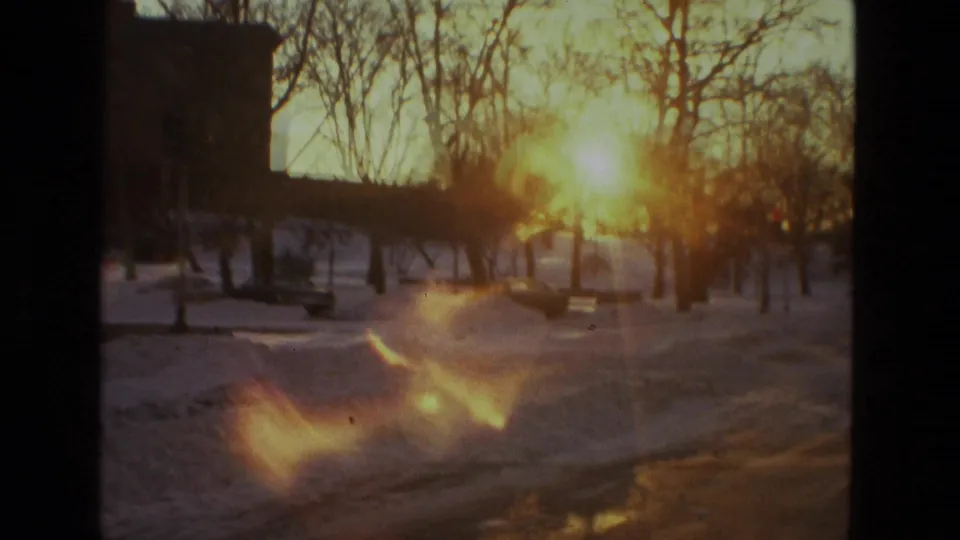 Warm sunset light flares through bare trees over snowy Drexel Hill streetscape at the end of the 1978 clip.