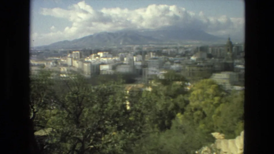 Elevated 1978 Granada panorama with pale urban blocks, leafy foreground, distant Sierra Nevada mountains, and partly cloudy sky.