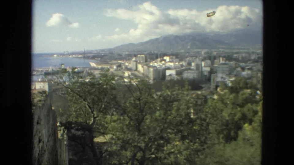 1978 8mm frame looking across Granada from a hillside, with trees in front, city blocks below, mountains behind, and water visible at left.