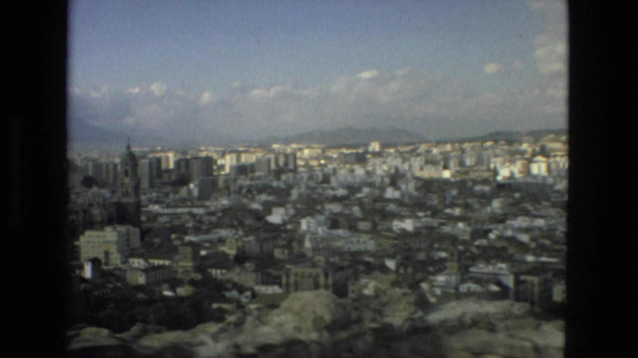 Wide city view from a rocky overlook with distant mountains and dark film borders.