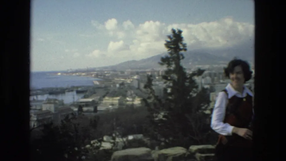 At the end of the pan, the woman is partly cropped at right while a tree, water, Granada buildings, and distant mountains fill the view.
