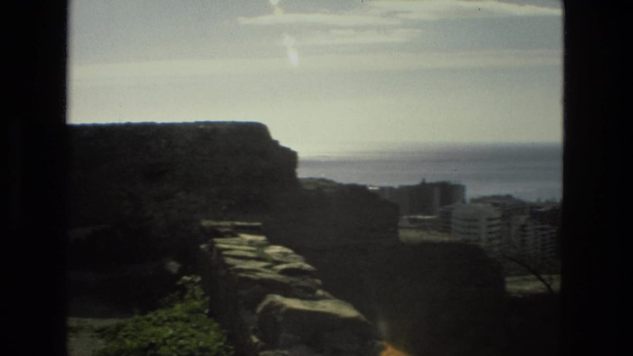 1978 Granada home-movie frame looking past dark stone ruins toward distant buildings and a pale horizon.