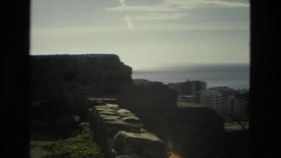 1978 Granada home-movie frame looking past dark stone ruins toward distant buildings and a pale horizon.